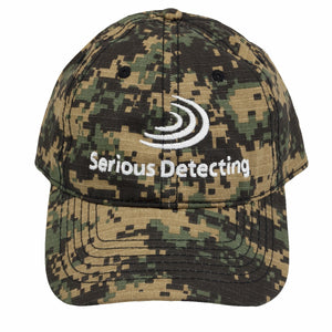 A camouflage baseball cap with the embroidered Serious Detecting logo on the front facing the front