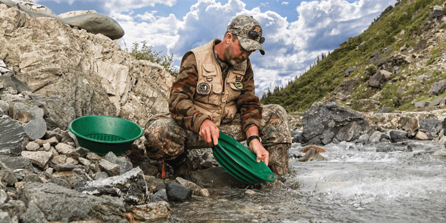 Prospector in stream on mountain side using basic gold panning equipment including a green riffled pan and a classifier