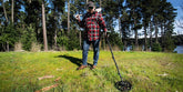 detectorist with X-TERRA Pro on near a lake with trees on green grass