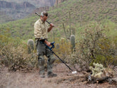Man using the Gold Monster 2000 metal detector with a detector tool on his should in the middle of a desert area 