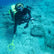 A female scuba diver with a camera and a PulseDive metal detector searching the ocean floor for lost treasure