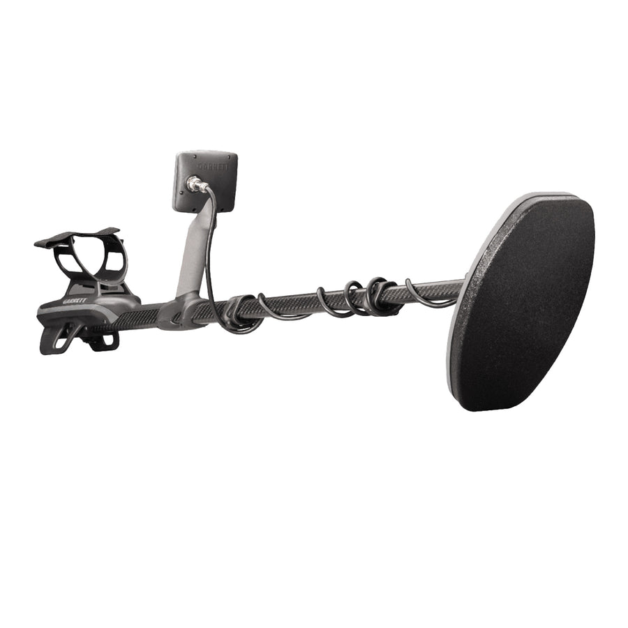 A black metal detector with a large coil, a textured handlebar grip, and a rectangular display screen, shown against a solid white background.