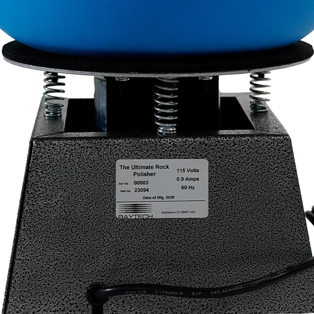Close-up of a rock polisher machine with a black textured base, silver springs, a blue grinding bowl, and a white product label reading 'The Ultimate Rock Polisher' with specifications.