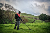 Person with a Minelab Manticore metal detector in a grassy field with hills and trees in the background