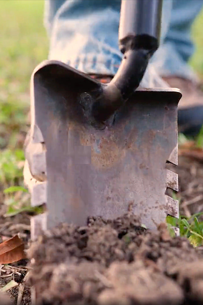 Close-up of a metal spade with a black handle in soil