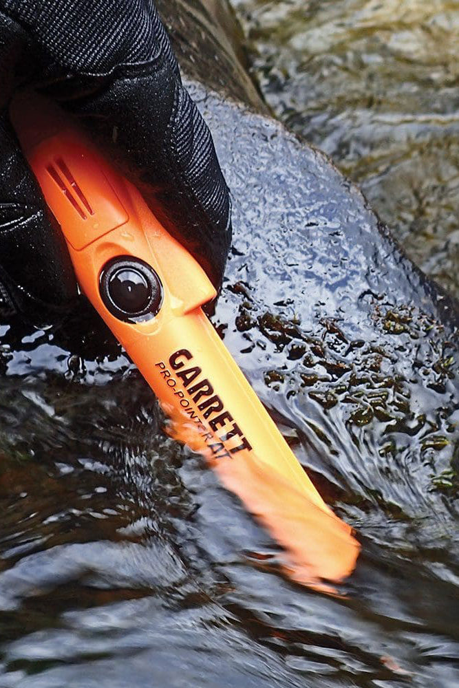 Orange Pro-Pointer 2 pinpointer metal detector held over water with a gloved hand, brand 'Garrett' visible