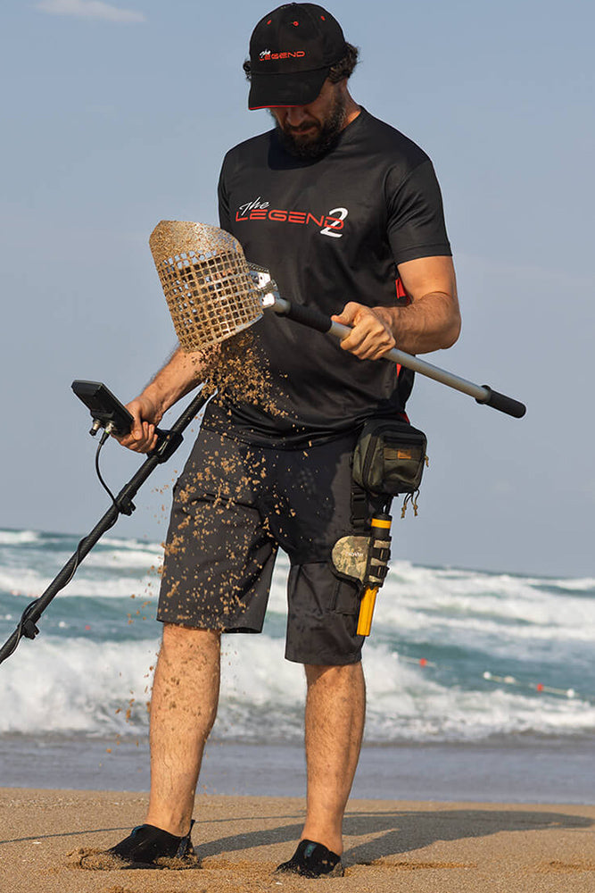 Person using a Nokta Legend 2 metal detector on a beach with ocean waves in the background