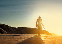 Person standing on a beach using a Nokta The Legend 2 Metal Detector with a sunset in the background