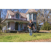 Detectorist swinging a Garrett ACE 400 on the lawn of an old two-story farmhouse
