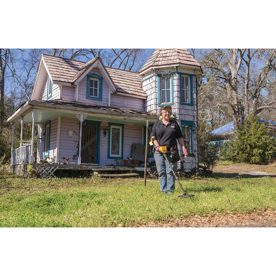 Detectorist swinging a Garrett ACE 400 on the lawn of an old two-story farmhouse
