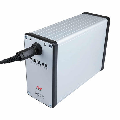 A Minelab lithium ion battery designed for powering metal detectors, with built-in amplifier. The battery is primarily silver with black and gray accents, featuring the Minelab brand logo and plugged in.