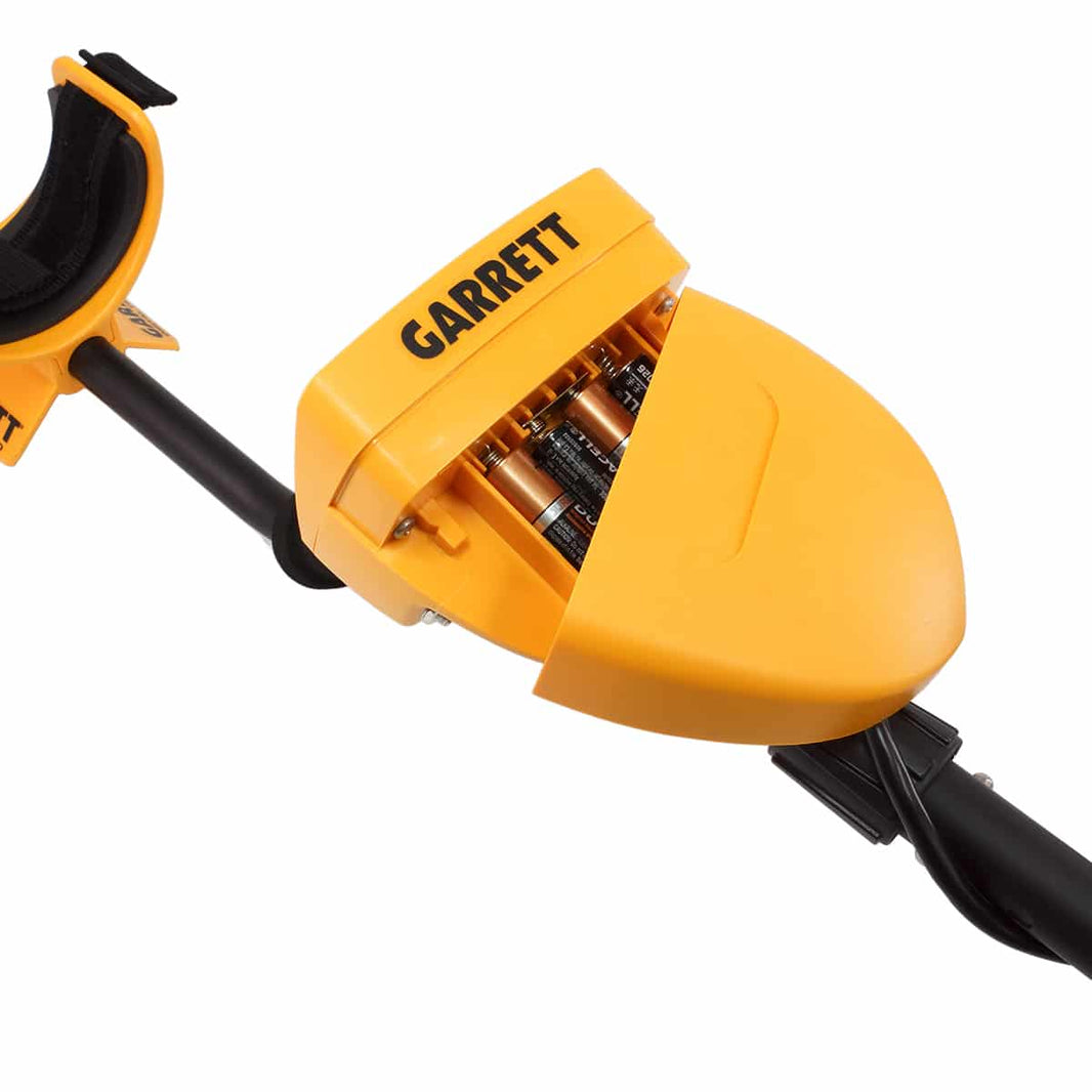 The yellow replacement Battery Cover for the Garrett ACE series Metal Detectors is shown partially off of the metal detector, revealing four double A batteries inside the control pod.  