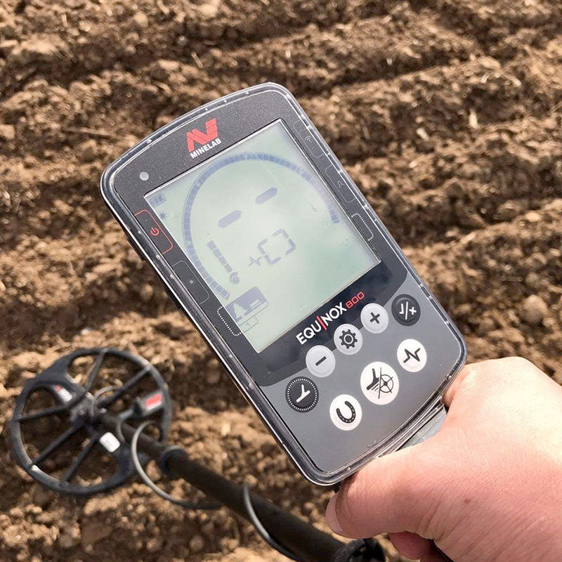 Close up of the Minelab EQUINOX 800 Multi-IQ Metal Detector control pod while the user scans a dirt field for objects. 