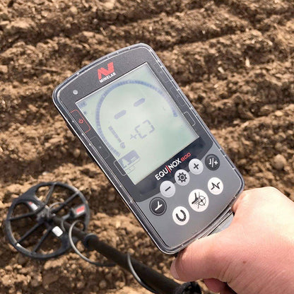 Close up of the Minelab EQUINOX 800 Multi-IQ Metal Detector control pod while the user scans a dirt field for objects. 
