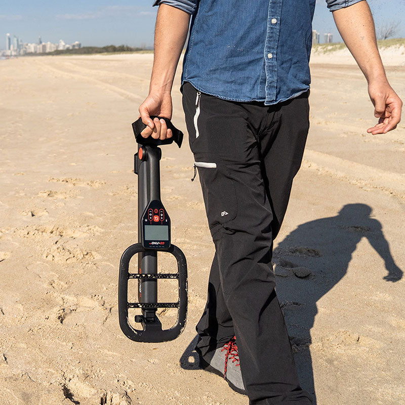Detectorist carrying the folded Minelab Go-Find 11 one-handed on the beach