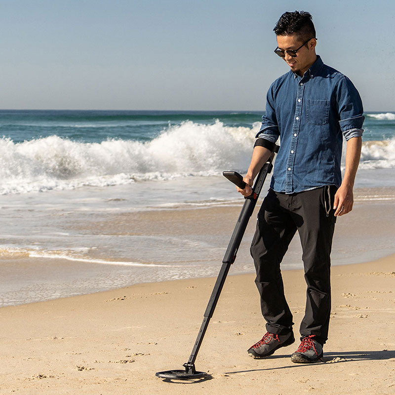 Man swinging the Minelab Go-Find 11 at the surf line on a sandy beach