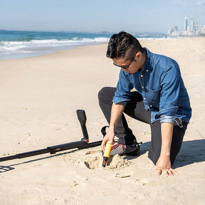 Detectorist recovering a target in beach sand with the Go-Find 11 laid beside the hole